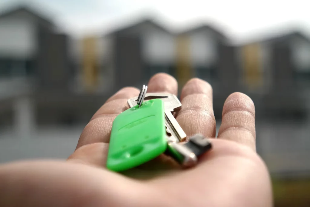Main tenant une clé verte devant des logements